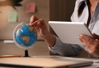 Unrecognizable businesswoman using digital tablet while examining globe and planning her vacation.